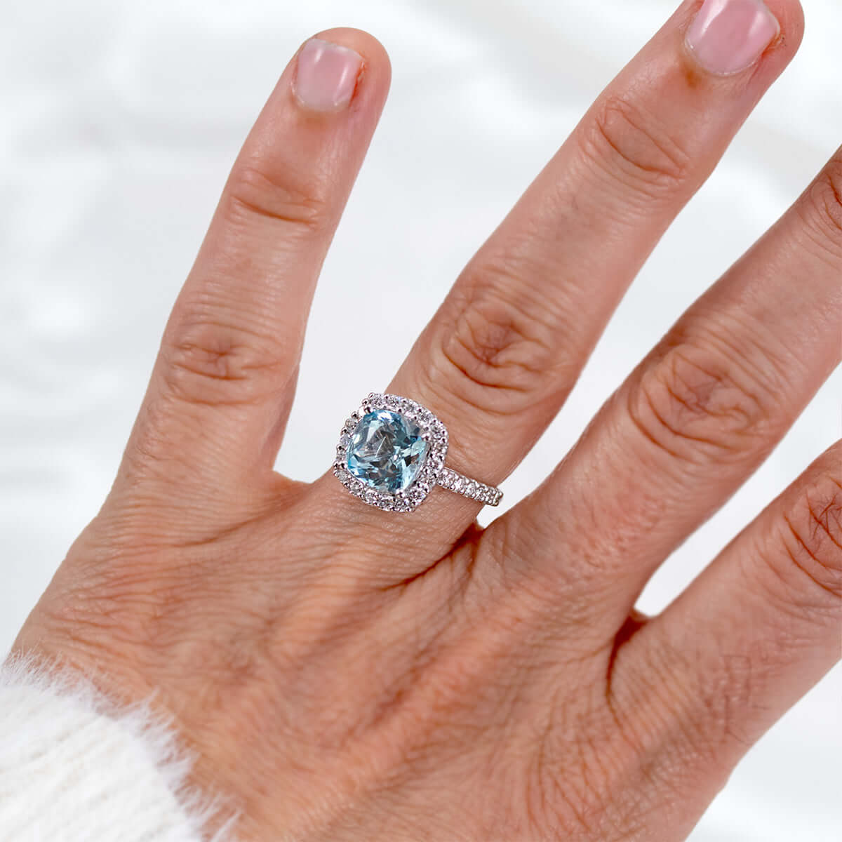 Elegant custom colored gemstone ring featuring a cushion-cut aquamarine with diamond halo on a hand.
