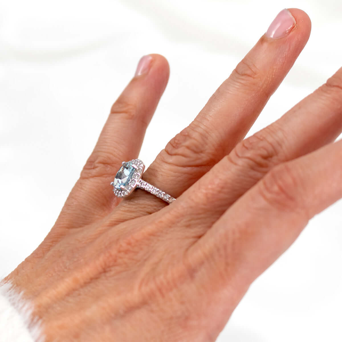 Elegant aquamarine ring with diamond halo displayed on a hand, showcasing custom colored gemstone beauty.
