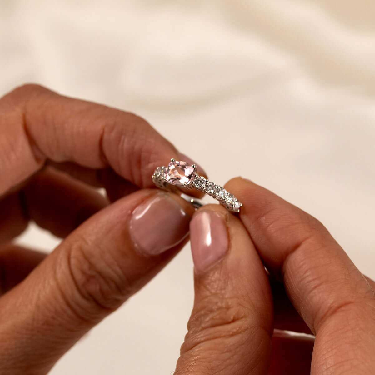 Elegant east-west pink morganite and diamond half-eternity ring held in hand, showcasing its sparkling beauty.