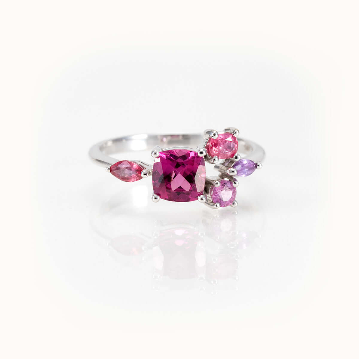 Elegant bespoke design ring featuring a cushion-cut pinkish purple garnet with sapphire side stones in 14kt white gold.