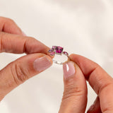 Hand holding an elegant bespoke design ring featuring pinkish purple garnet and sapphire side stones in white gold.