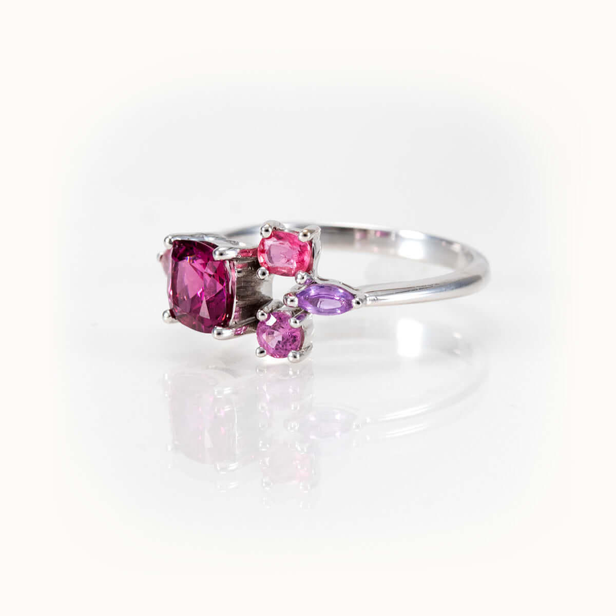 Elegant bespoke design ring featuring pinkish-purple garnet flanked by sapphires in timeless 14kt white gold.