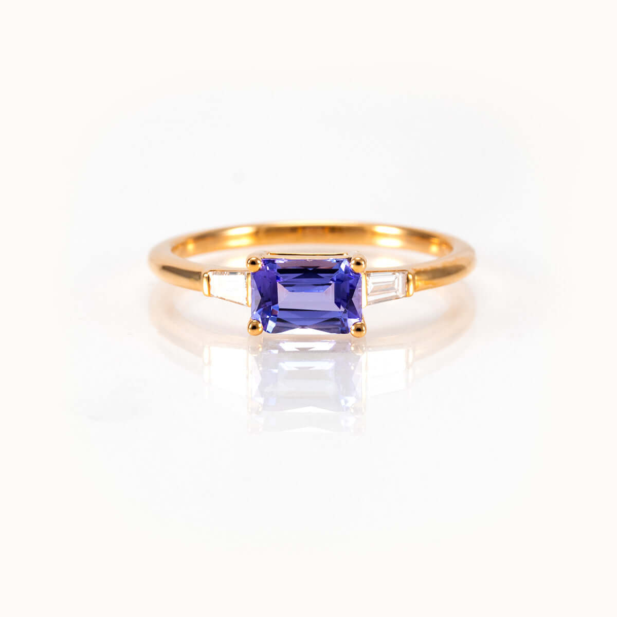 Light blueish-purple tanzanite east-west ring in 14K yellow gold with tapered baguette diamonds, bespoke design.