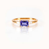 Light blueish-purple tanzanite east-west ring in 14K yellow gold with tapered baguette diamonds, bespoke design.